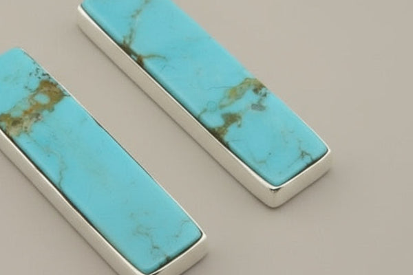 Two turquoise stone inlays with silver frames on a beige background