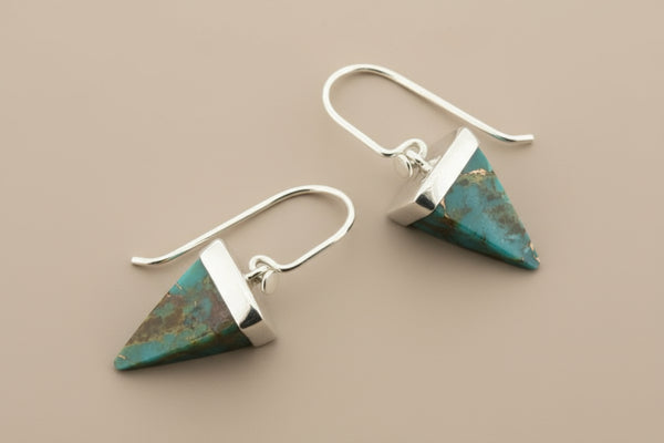 Pair of silver and turquoise triangle-shaped earrings on a gray background
