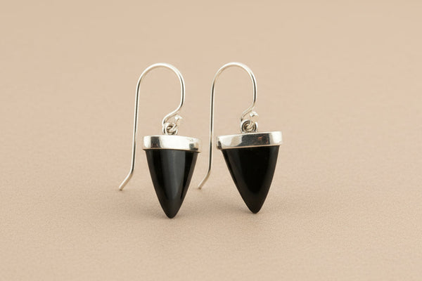 Black spearhead-shaped earrings with silver accents on a gray background