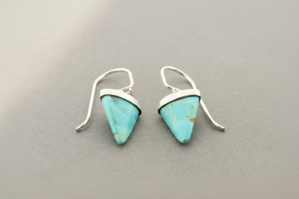Turquoise triangle earrings with silver hooks on a gray background