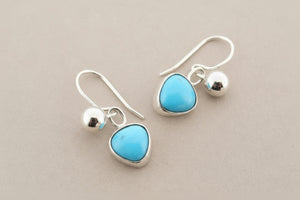 Turquoise teardrop earrings with silver hooks on a gray background