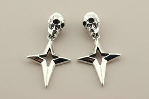 Pair of silver skull and star-shaped earrings on a beige background
