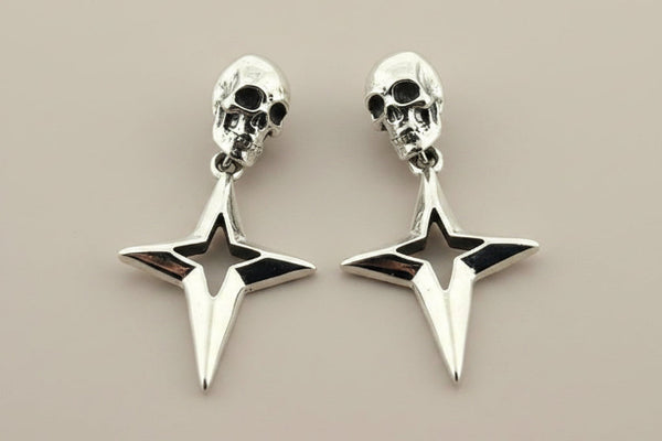 Pair of silver skull and star-shaped earrings on a beige background