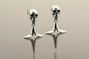 Silver skull and star-shaped earrings on a reflective surface with a neutral background