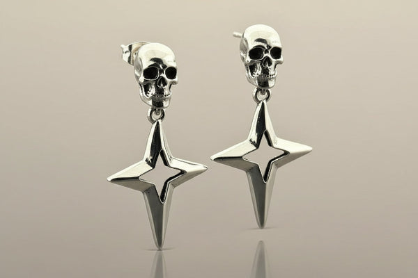 Silver skull and star-shaped earrings on a reflective surface with a neutral background