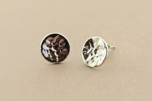 Two round silver earrings with textured surfaces on a gray background