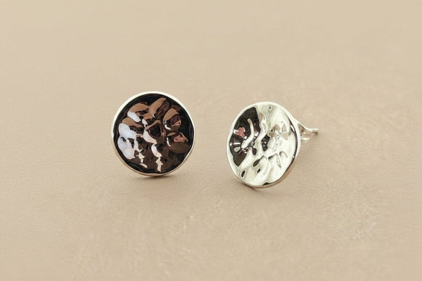 Two round silver earrings with textured surfaces on a gray background