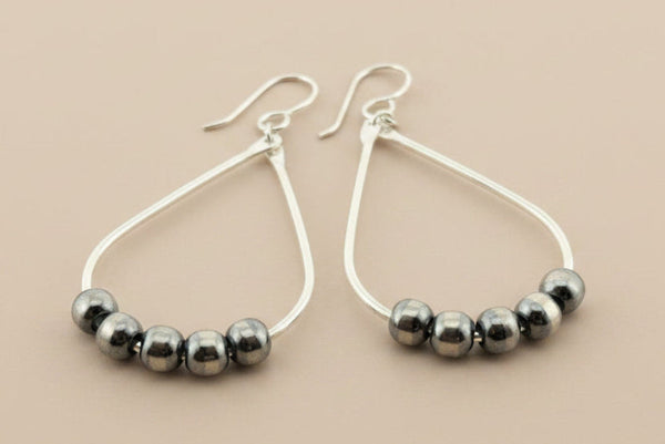 Teardrop-shaped earrings with black and silver beads on a gray background