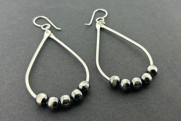 Teardrop-shaped earrings with striped beads on a gray background