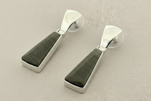 Pair of earrings with green stone and silver metal on a gray background