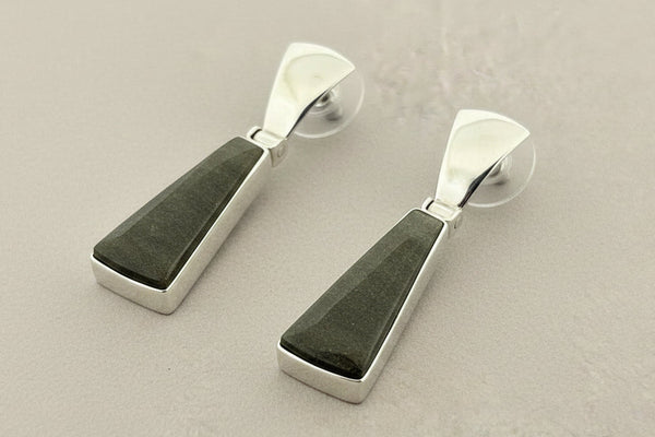 Pair of earrings with green stone and silver metal on a gray background