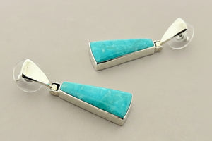 Pair of earrings with turquoise stones and silver settings on a gray background