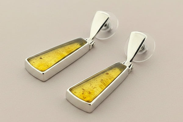 Pair of earrings with yellow center and silver frame on a gray background