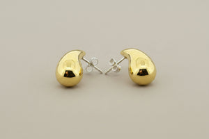 A pair of polished gold crescent moon stud earrings with silver post backs, displayed on a textured dark gray background.