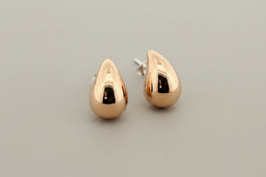 A pair of polished rose gold crescent-shaped stud earrings with butterfly backings, displayed on a textured dark gray surface.