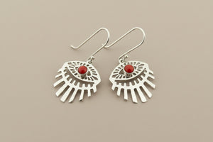 A pair of sterling silver dangle earrings with a fan-like cutout design and a small round red stone in the center, displayed on a dark gray textured background.