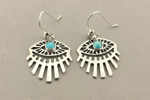 A pair of silver-toned dangle earrings with a fan or sunburst cutout design and a small round turquoise stone at the center, shown on a dark gray background.
