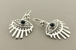 A pair of sterling silver dangle earrings with a stylized eye design, featuring a black onyx stone in the center of each earring, displayed on a dark gray background.