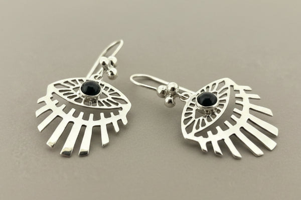A pair of sterling silver dangle earrings with a stylized eye design, featuring a black onyx stone in the center of each earring, displayed on a dark gray background.