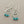 Load image into Gallery viewer, A pair of silver dangle earrings with heart-shaped filigree centers and three small turquoise beads hanging from each earring, displayed on a dark gray textured surface.
