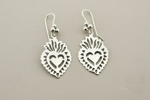A pair of silver heart dangle earrings with cutout details and a small red heart accent, displayed on a dark gray textured background.