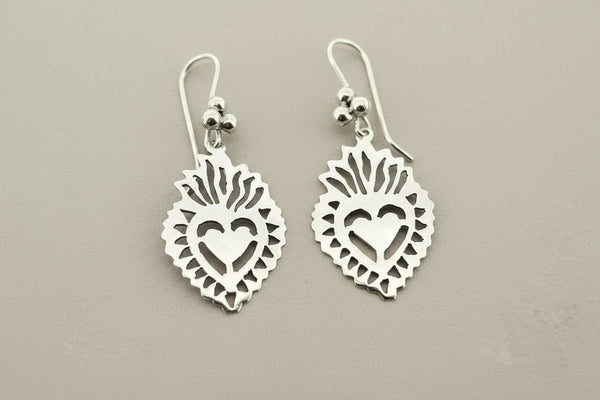 A pair of silver heart dangle earrings with cutout details and a small red heart accent, displayed on a dark gray textured background.