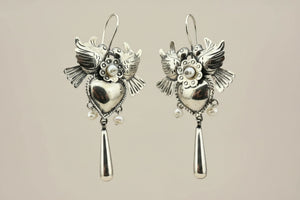A pair of silver owl dangle earrings with small pearl-like beads, shown on a dark gray background.