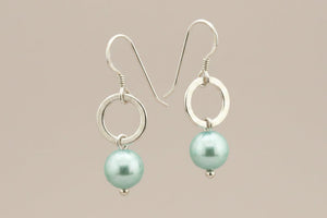 Pair of earrings with light blue pearls  and silver loops on a beige background