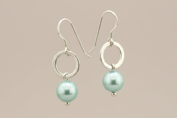 Pair of earrings with light blue pearls  and silver loops on a beige background