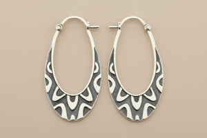 Pair of silver hoop earrings with intricate patterns on a gray background