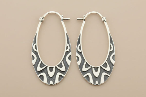 Pair of silver hoop earrings with intricate patterns on a gray background