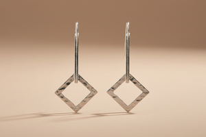 Pair of silver square earrings on a beige background
