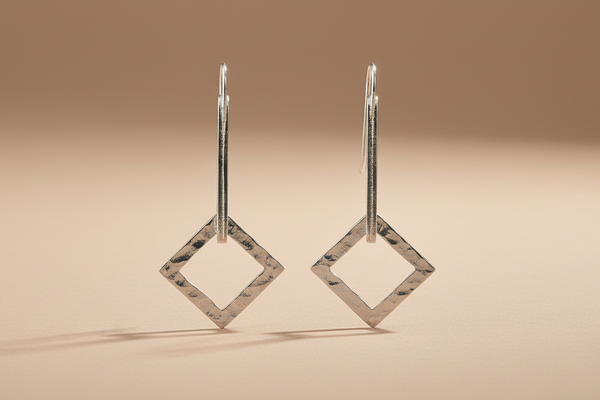 Pair of silver square earrings on a beige background