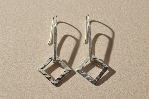 Pair of silver square earrings on a beige background