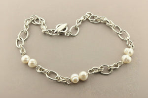 Silver chain bracelet with white pearls on a gray background