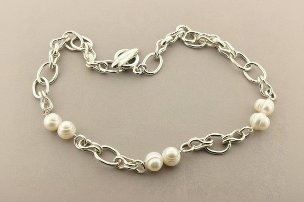 Silver chain bracelet with white pearls on a gray background