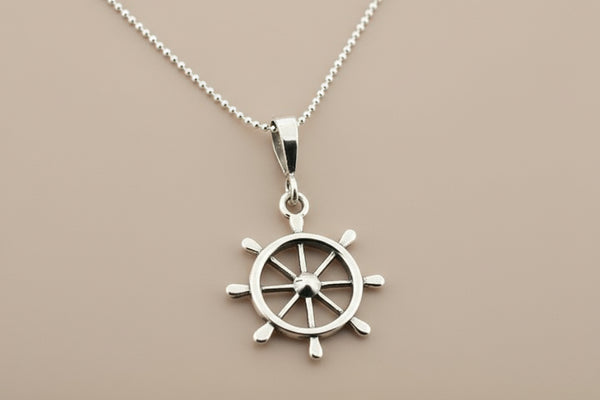 Silver ship's wheel pendant on a chain against a gray background