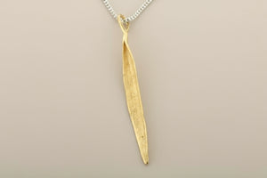 Gold leaf-shaped pendant on a chain against a gray background