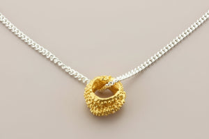 Gold pendant on a silver chain against a gray background