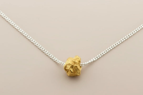 Gold necklace pendant on a silver chain against a gray background