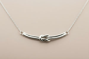 Silver necklace with a knot design on a gray background