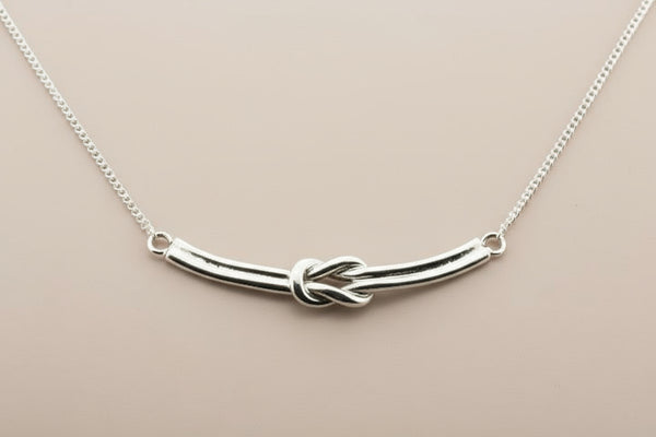 Silver necklace with a knot design on a gray background