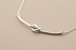 Silver necklace with a knot design on a gray background
