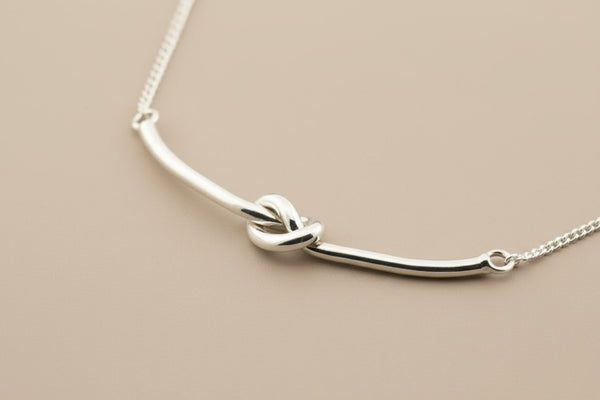 Silver necklace with a knot design on a gray background