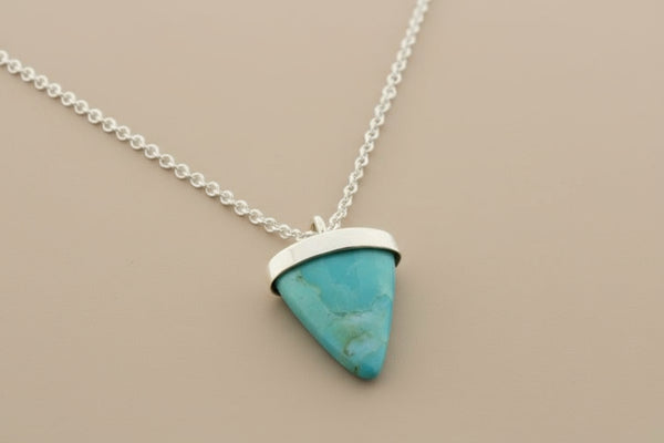 Turquoise triangle pendant on a silver chain against a gray background