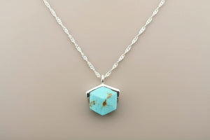 Turquoise hexagonal pendant necklace on a gray background