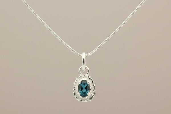 Silver pendant with a blue gemstone on a gray background