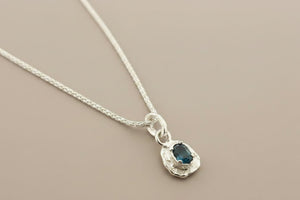 Silver necklace with a blue gemstone pendant on a gray background