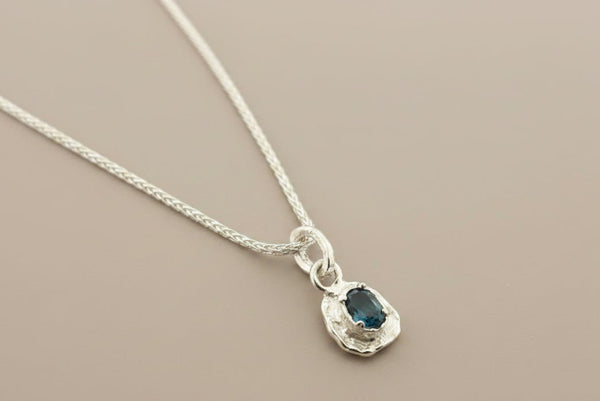 Silver necklace with a blue gemstone pendant on a gray background