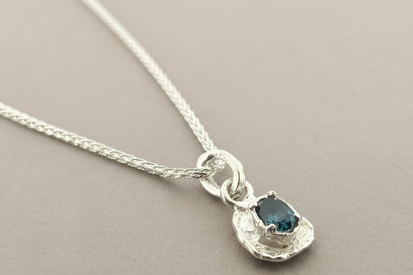 Silver necklace with a pendant featuring a blue gemstone on a gray background